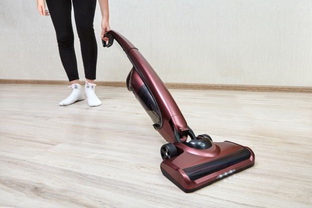 Cleaning lady in black leggings cleans dust in an empty room using a cordless handheld vacuum with led lights on