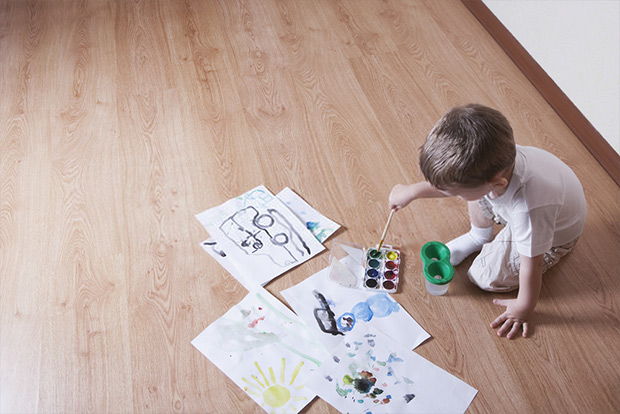 Elevated view of young boy painting with watercolors and paintbrush on laminated floor