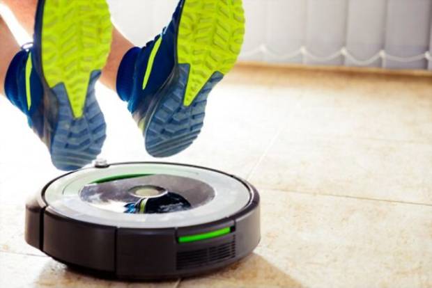 A picture showing someone’s shoes near a Roomba gadget