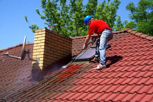 A close picture of a man cleaning his roof using a pressure washer