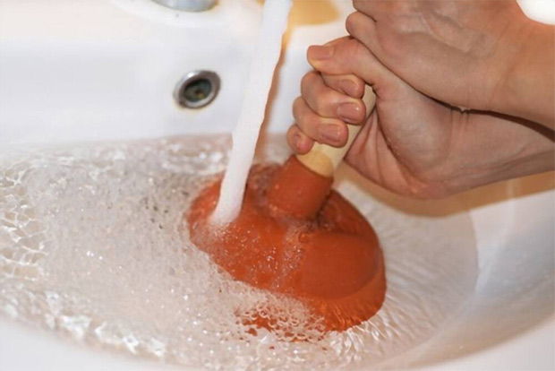 A picture of  a woman trying to clean her sink drain