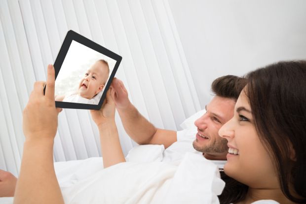 A picture showing two parents monitoring their baby on bed