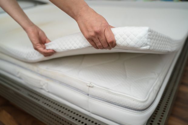 Hands laying a mattress topper on a bed