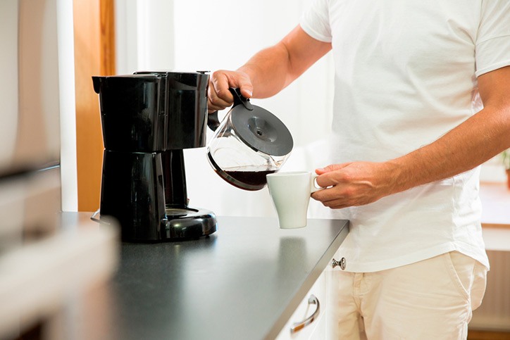 Man in the kitchen pouring a mug of hot filtered coffee from a glass pot