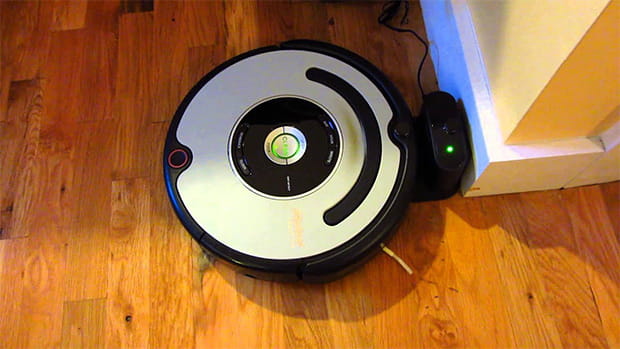 A Roomba machine is charging at its station